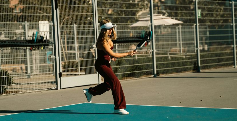 A woman playing tennis on a blue court, wearing a white visor and brown outfit, preparing to hit the ball.