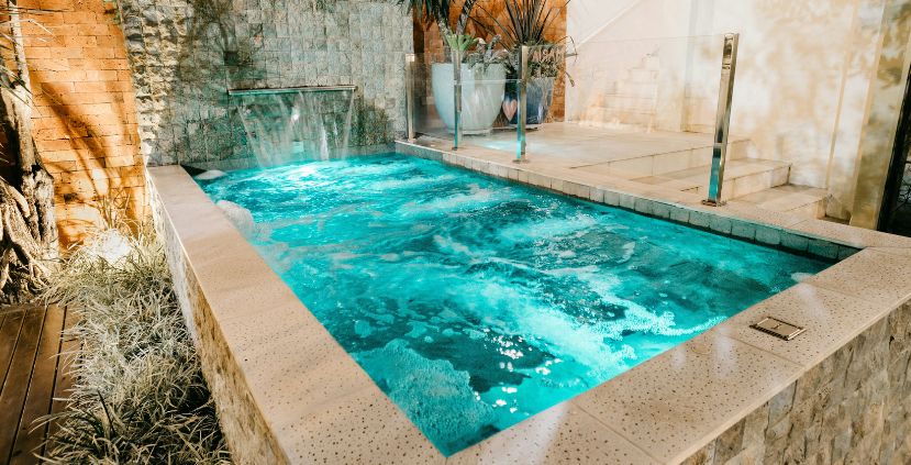A serene spa pool with bubbling turquoise water, surrounded by stone walls and plants.