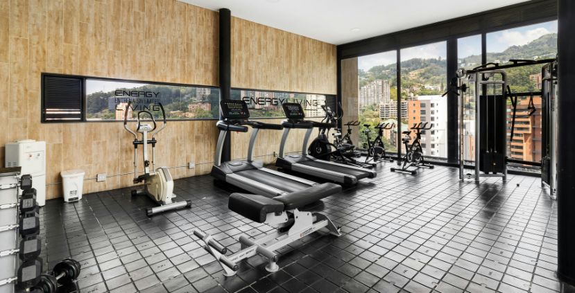 A bright gym with exercise equipment, large windows, and views of a cityscape.