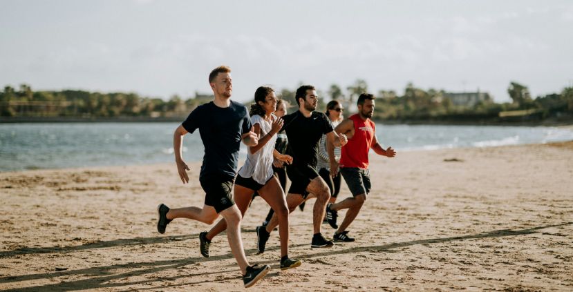 Five people running on a sandy beach near the water. They are wearing athletic clothing.