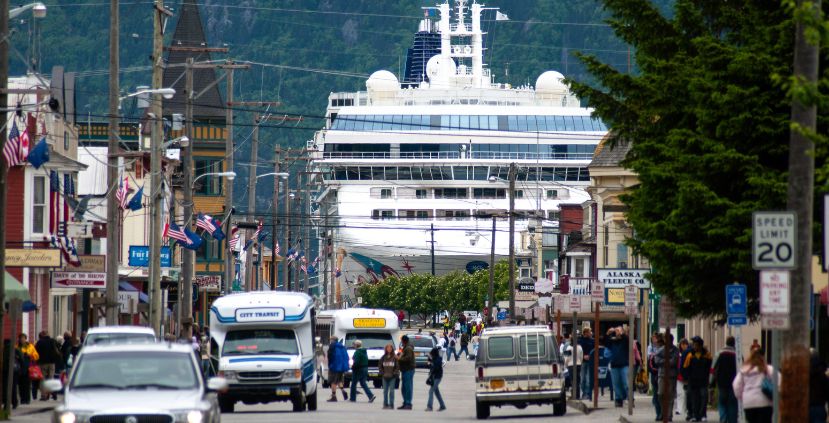 A busy street with cars and people, featuring a large cruise ship in the background.