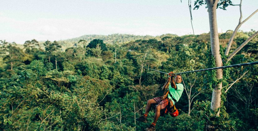 A male on a zip line above a lush green forest, enjoying an adventure in nature.