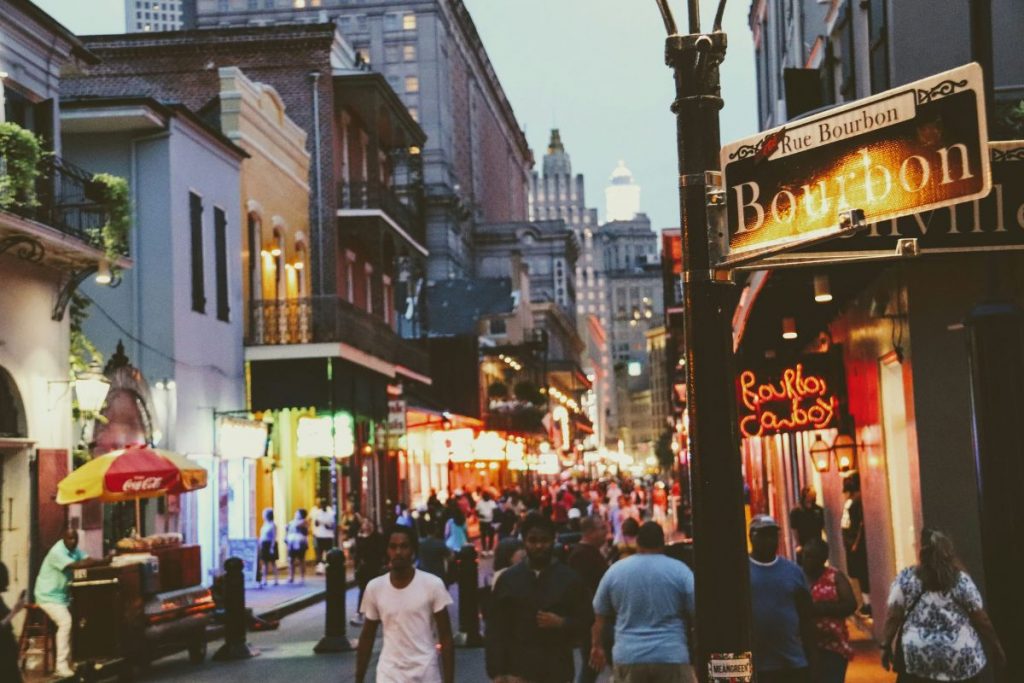 Busy Bourbon Street in New Orleans, with crowds and colourful lights at dusk.