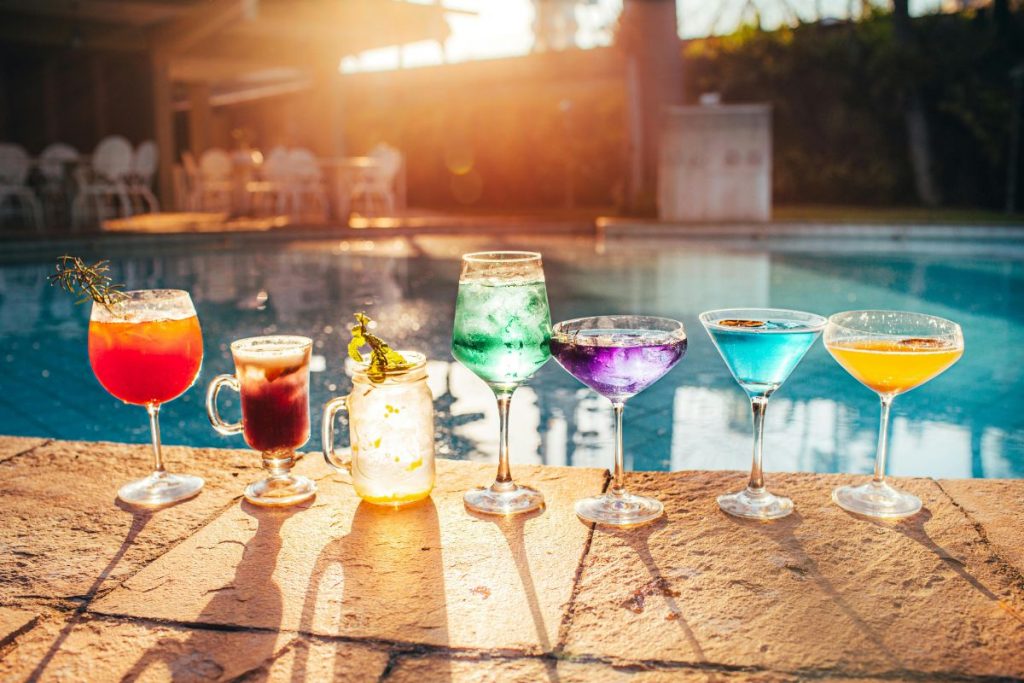 Luxury resort swimming pool with palm trees, footbridge, and clear blue sky at a coastal holiday destination