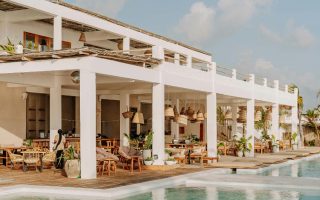 Open-air restaurant and pool area at a modern resort with white architecture and wooden terraces